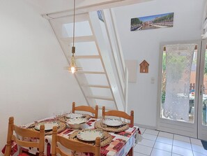 A dining area with a table set for four, a wooden chair, a hanging light fixture, and a view through a glass door. - Les Villas sur la Colline by Interhome (Narbonne-Plage)