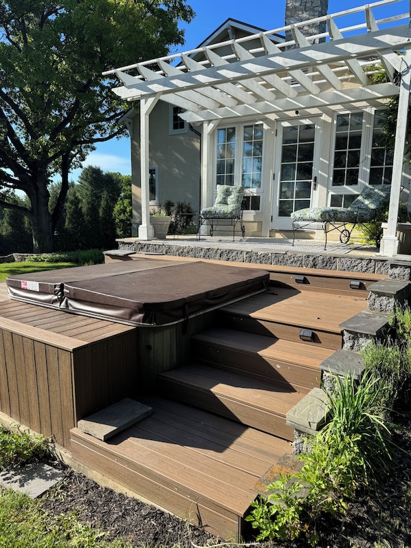 Eine überdachte Terrasse im Freien mit Whirlpool, Treppen und einer Pergola.
