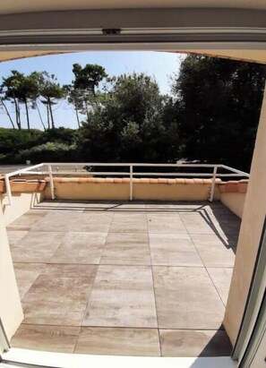 A view through a glass door of a balcony with tiled flooring, a white railing, and a view of trees and sky. - VILLA ROSAMUNDE (Jard-sur-Mer)