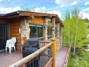 A wooden deck with a barbecue grill, a covered seating area, and a stone wall. - King Davis House-Best Views in Mt. Crested Butte (Crested Butte)
