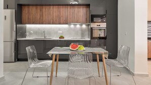Une cuisine moderne avec des meubles de couleur sombre, un mur d’accent en bois et une table en verre accompagnée de chaises.