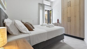 Une chambre à coucher avec un lit, des oreillers, une table de chevet, une lampe, une fenêtre avec des rideaux et une armoire en bois.