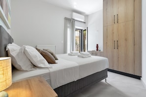 Ein Schlafzimmer mit Bett, Kissen, Nachttisch, Lampe, einem Fenster mit Vorhängen und einem Holzschrank.