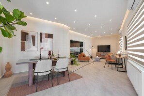 Ein modernes Wohnzimmer mit Essbereich, einer K üche im Hintergrund und einem an der Wand befestigten Fernseher.