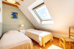 Ein Zimmer mit schrägem Dach, zwei Betten, einem Sessel, einem Nachttisch, einer Lampe, einem Gemälde und einem Oberlicht.