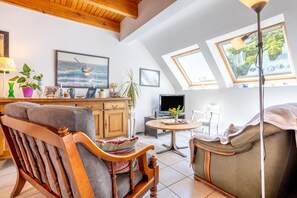 Ein gemütliches Wohnzimmer mit einem Holzstuhl, einer Couch, einem Fernseher und einem Tisch mit einer Pflanze.