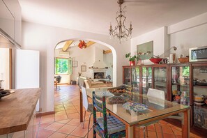 Een eetruimte met een glazen tafel, stoelen, een kroonluchter en een keuken op de achtergrond.