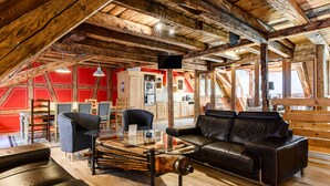 Um amplo loft com teto alto, vigas de madeira aparentes, cozinha moderna e aconchegante área de estar com sofás de couro e mesa de centro de vidro.
