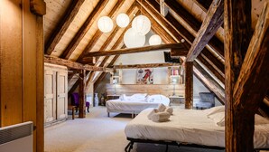 Quarto com vigas de madeira, duas camas, uma escrivaninha e uma cadeira.