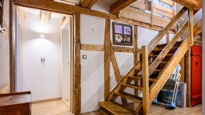 Uma escada de madeira com corrimão, uma porta que dá para outro cômodo e um quadro na parede.