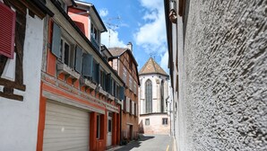 Uma rua estreita com edifícios de ambos os lados, uma igreja com telhado pontiagudo e um céu claro.