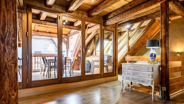 Interior em madeira com escada, cômoda branca e abajur.