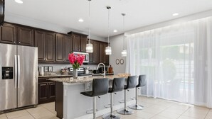 A modern kitchen with a central island, bar stools, stainless steel appliances, and pendant lighting. - 6BR Disney Escape Pool, SPA and fun (Kissimmee)