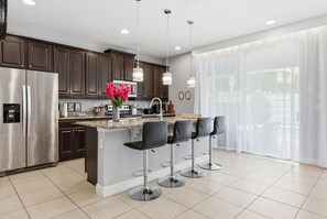 A modern kitchen with a central island, bar stools, stainless steel appliances, and pendant lighting. - 6BR Disney Escape Pool, SPA and fun (Kissimmee)