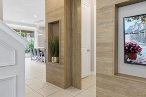A hallway with a wooden door, a framed picture of a landscape, and a potted plant. - 6BR Disney Escape Pool, SPA and fun (Kissimmee)