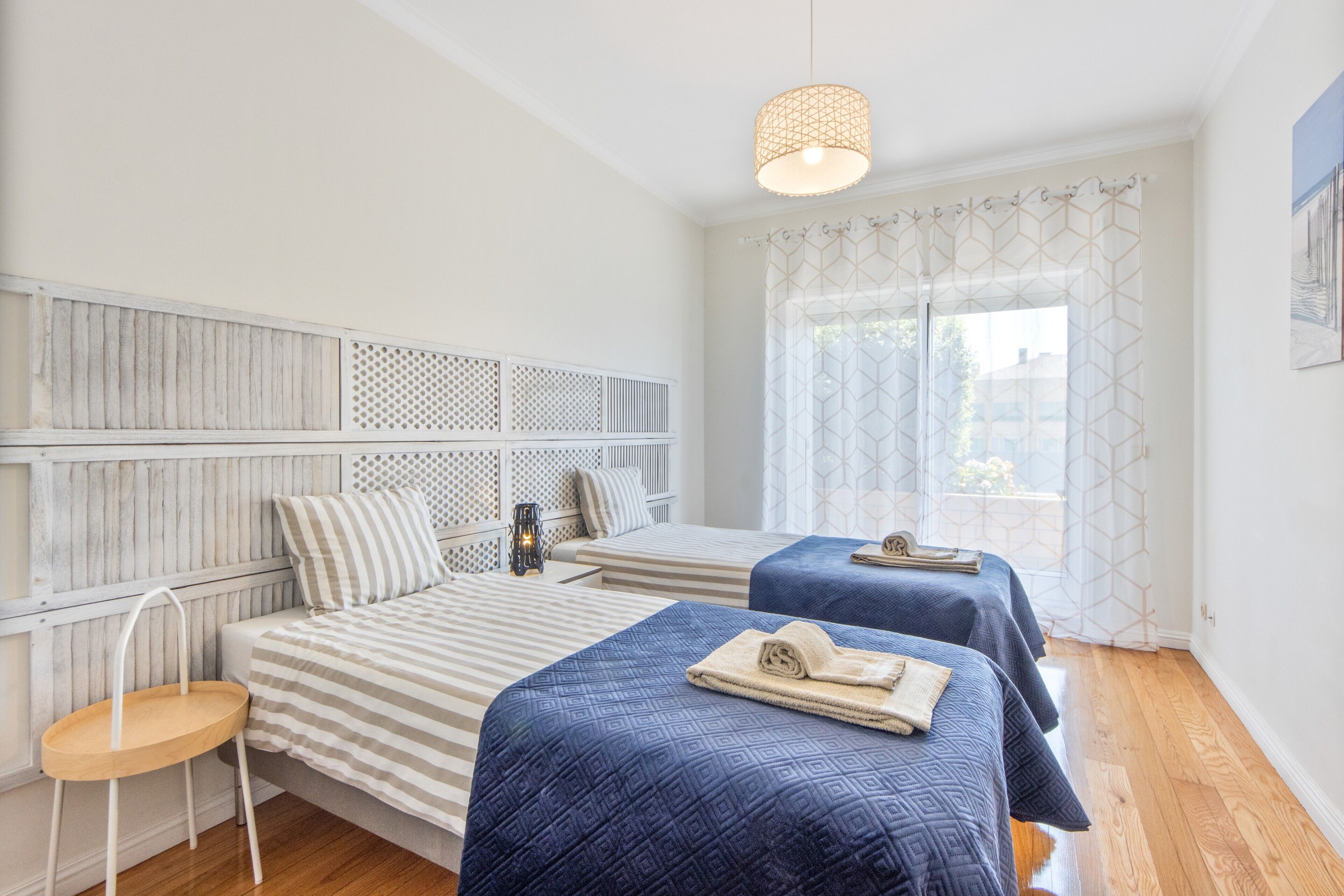 Een hotelkamer met twee bedden, een tafeltje, een stoel en een raam met gordijnen met een patroon.