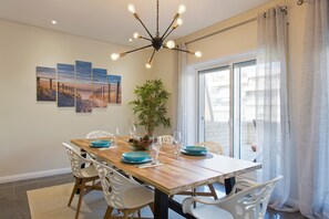 A dining area with a wooden table, white chairs, a potted plant, and a modern chandelier. - Beach Sunset – Oceanfront Apartment with Terrace and Sea View (Vila Nova de Gaia)