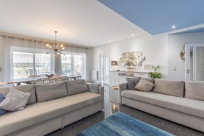 Ein modernes Wohnzimmer mit einer Sofagarnitur, einem Essbereich mit Tisch und Stühlen sowie einer Küchenzeile mit Herd und Schränken.