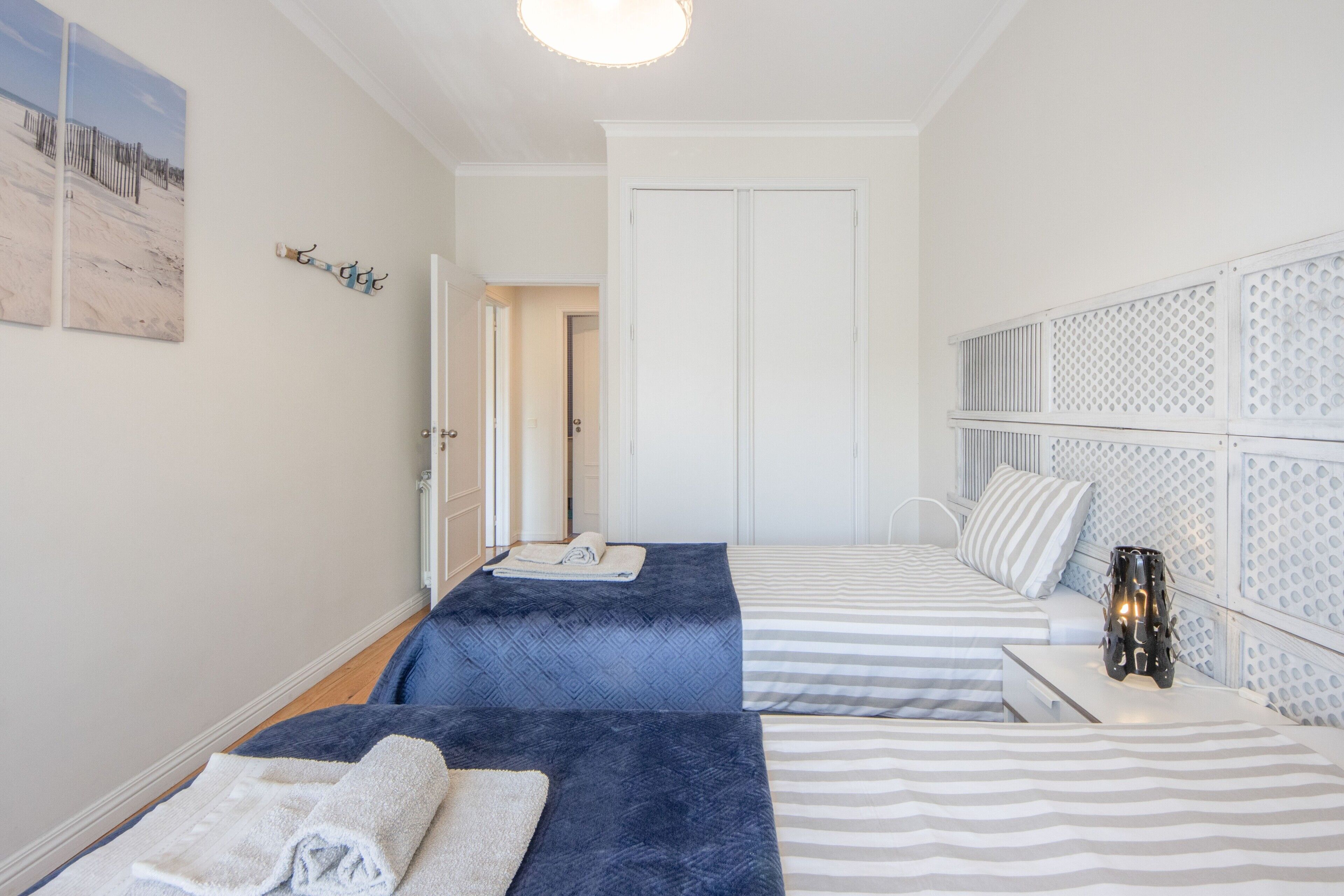 A hotel room with two beds, a white door, and a wall-mounted light fixture.