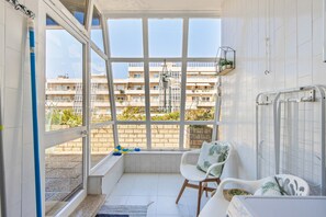 A balcony with a view of a building, a chair, a small table, and a radiator. - Beach Sunset – Oceanfront Apartment with Terrace and Sea View (Vila Nova de Gaia)