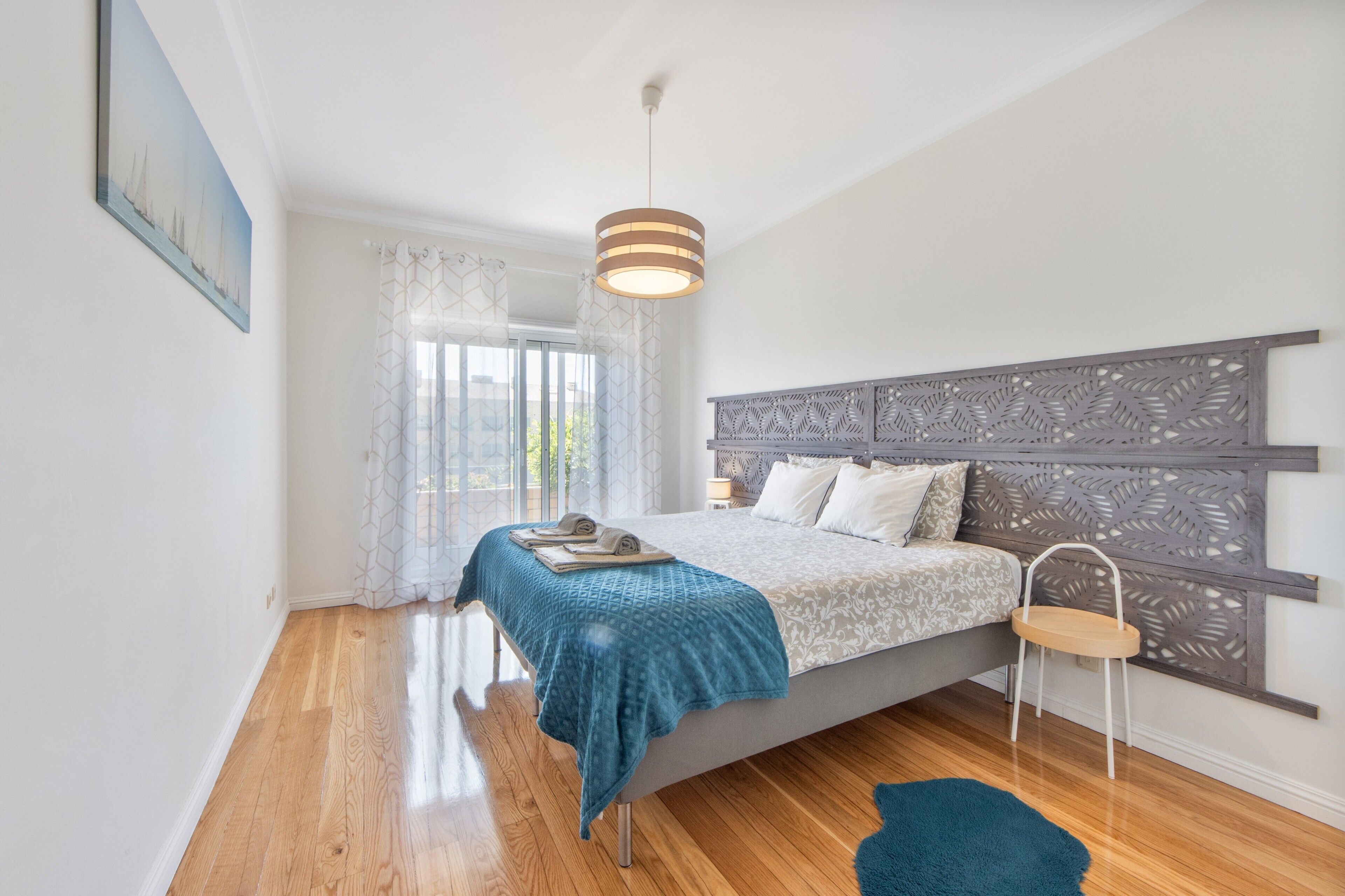 A bedroom with a bed, a nightstand, a chair, a window with curtains, and a ceiling light.