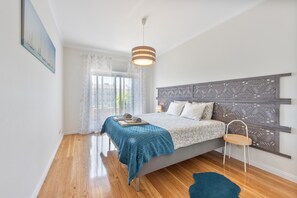 Une chambre à coucher comprenant un lit, une table de chevet, une chaise, une fenêtre avec des rideaux et un luminaire au plafond.