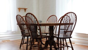 A dining table with four wooden chairs, a wooden floor, and a white wall with a wooden shelf. - Country Oasis 4-bedroom farmhouse in tranquil Shelby with cozy charm (Shelby)