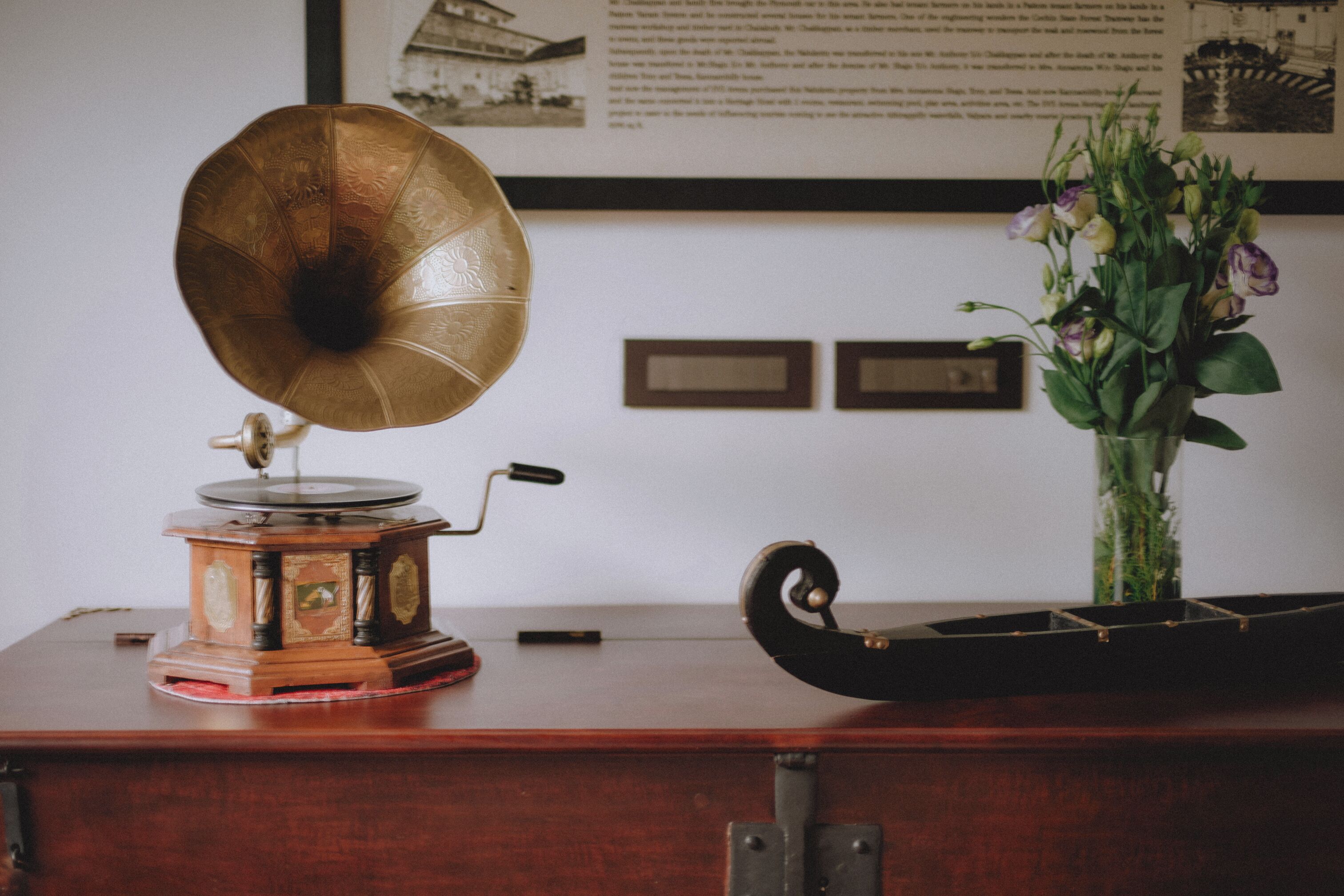 Un tocadiscos antiguo sobre una mesa de madera, con un jarrón de flores y cuadros en la pared.