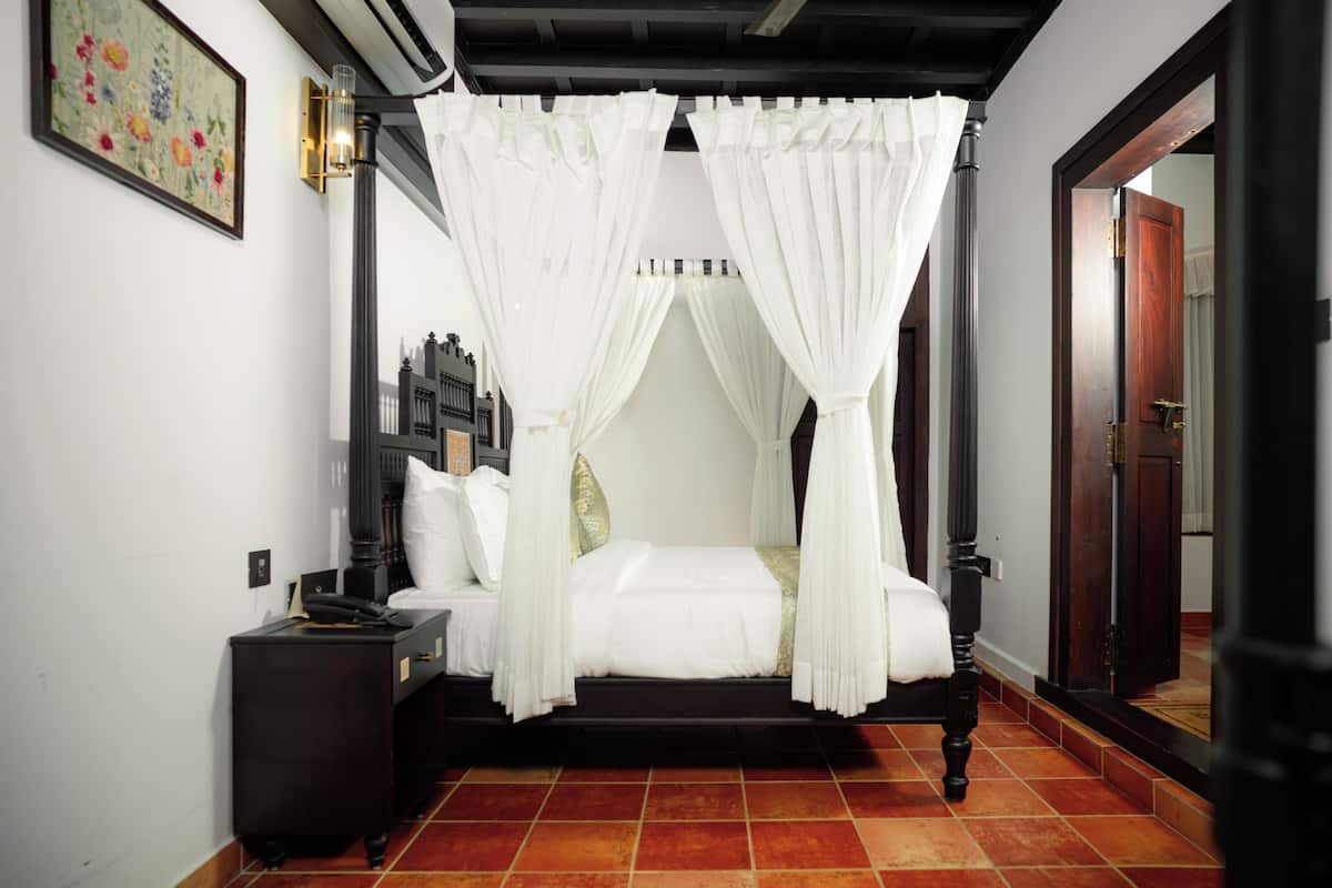 A four-poster canopy bed with white bedding, a nightstand, and a wall-mounted lamp.