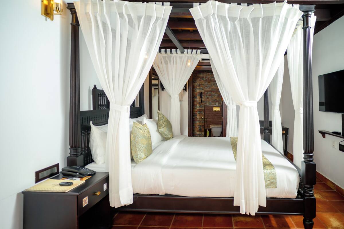 A four-poster bed with white canopy, a nightstand with a telephone, and a brick wall in the background.