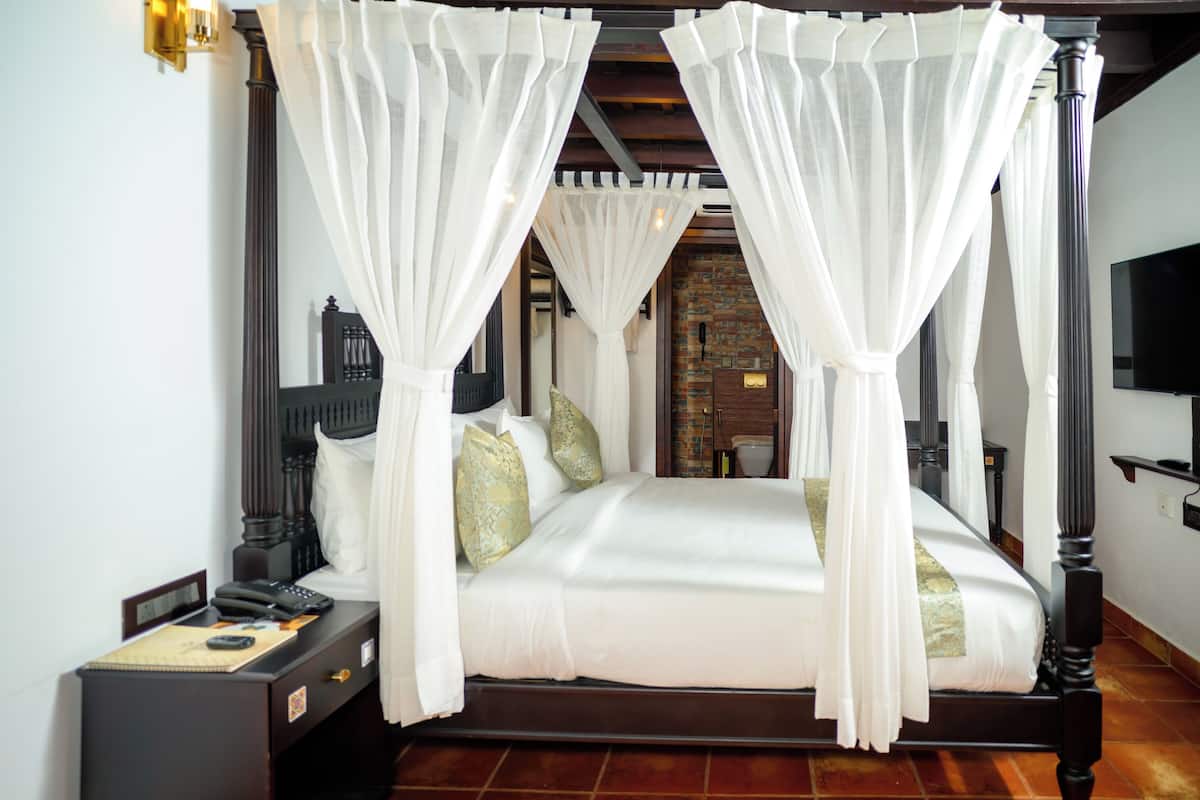 A four-poster bed with white canopy, a nightstand with a telephone, and a brick wall in the background.