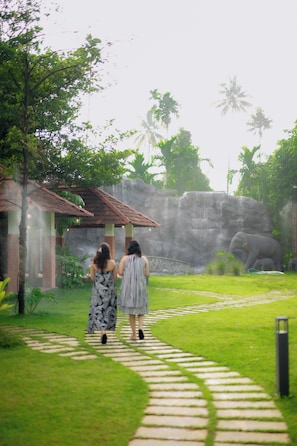 A pathway leading to a building with a tiled roof, surrounded by greenery and a large rock formation.