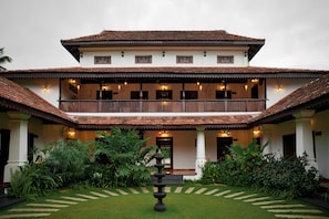 A two-story building with a balcony, a garden with a stone pathway, and a traditional tiled roof.