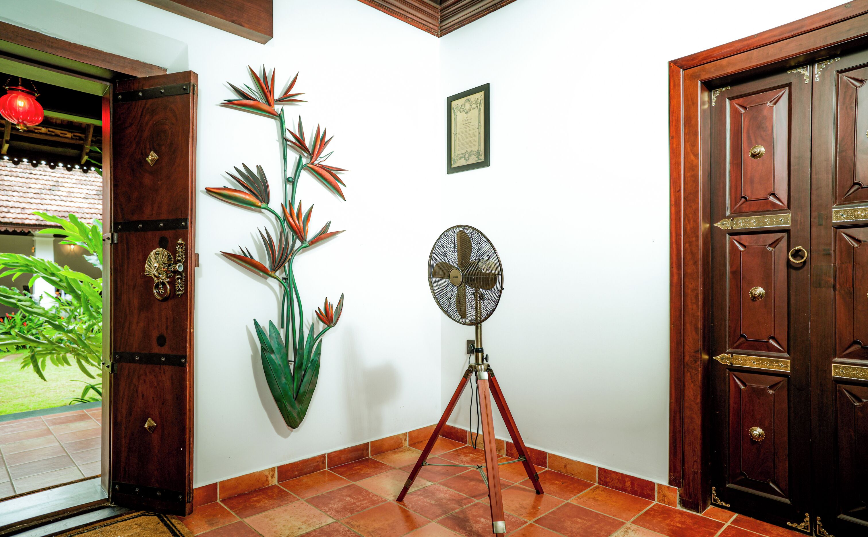Una habitación con puerta de madera, un ventilador de pared y una planta decorativa.