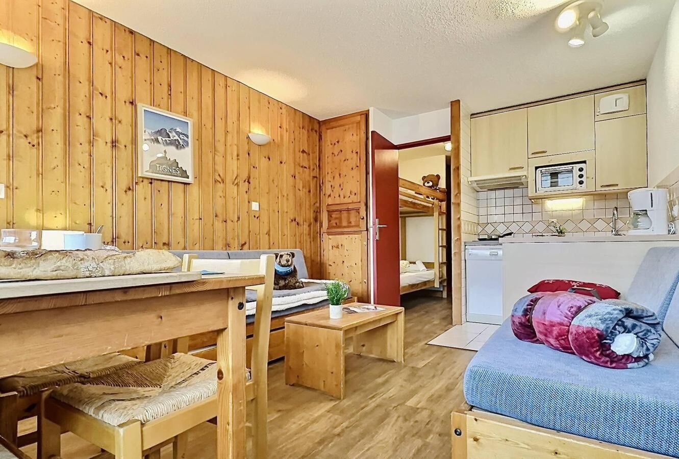 A wooden-paneled room with a dining table, chairs, a sofa, and a kitchenette.