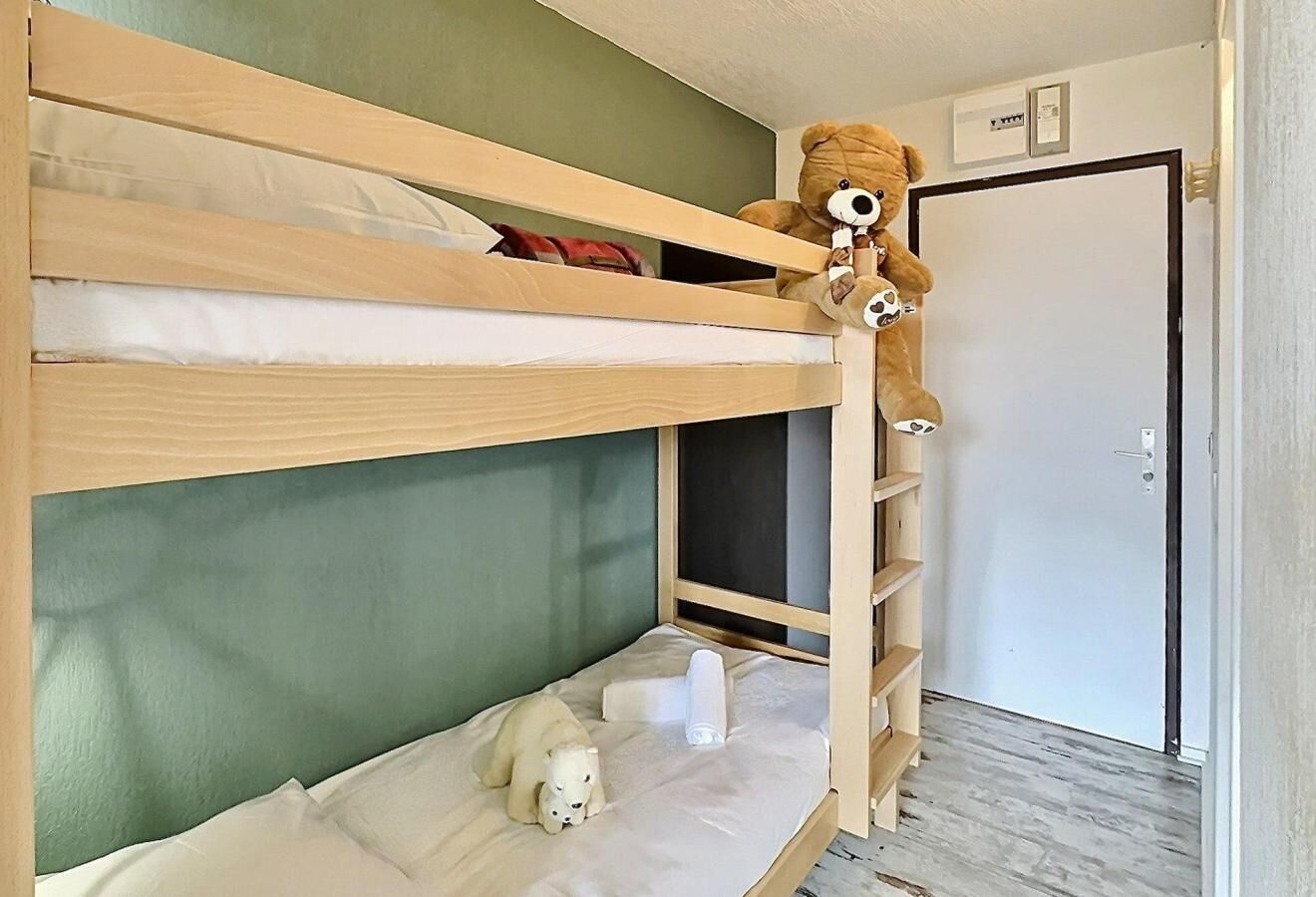 A bunk bed with a teddy bear on the top bunk and a small white dog on the bottom bunk.
