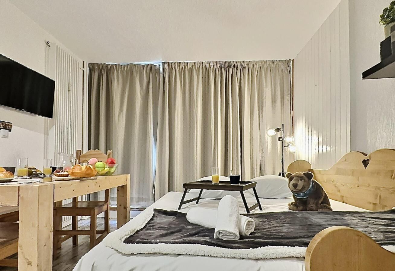 A bedroom with a bed, a wooden desk, a chair, a bedside table with a tray, and a dog.