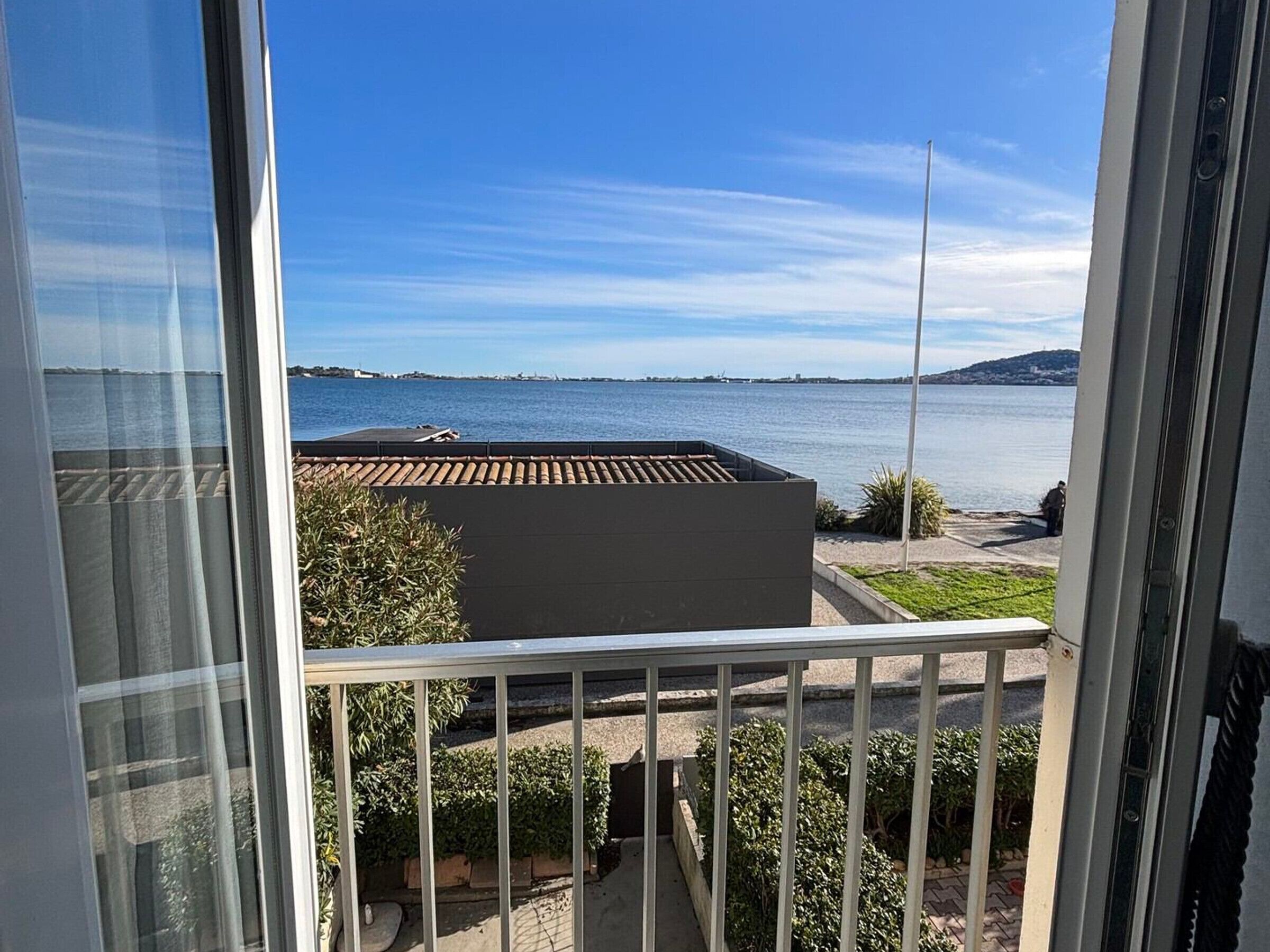 Ein Balkon mit Meerblick, ein Gebäude mit Ziegeldach und eine Rasenfläche.