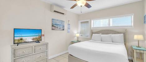 A bedroom with a bed, a ceiling fan, a television, a dresser, and a window with blinds.