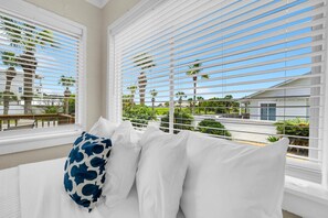 A hotel room with a bed, white blinds, and a view of palm trees and buildings. - Linda's Cozy Collection (Panama City Beach)