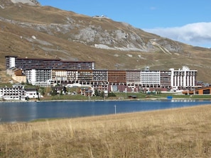 Ein Hotel mit mehreren Stockwerken, einem See im Vordergrund und einer Bergkulisse.