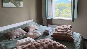 A bedroom with a bed, pillows, a painting, and a window with a view.