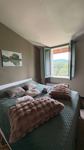 Ein Schlafzimmer mit Bett, Kissen, einem Bild und einem Fenster mit Blick.