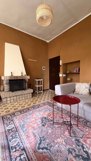 Ein Wohnzimmer mit Kamin, einem gemusterten Teppich, einem roten Sessel und einem Sofa.