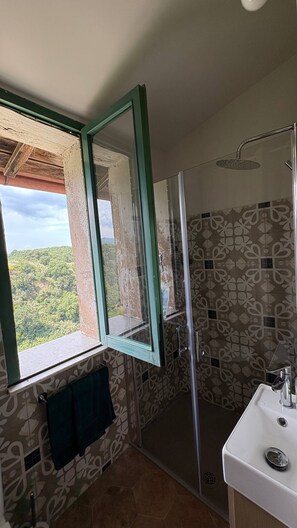 A bathroom with a shower, a sink, a window with a view of greenery, and patterned tiles. - A true Italian delight on a hill in the center of Italy, amazing views (Vignanello)