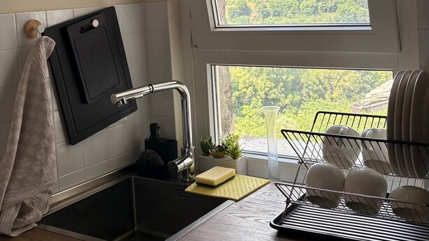 A kitchen with a window, a sink, a cutting board, and a dish rack.
