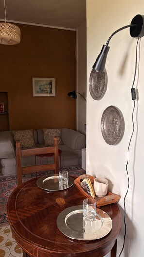 Ein Esstisch mit Tablett, Kerze und Tasse. Im Hintergrund befindet sich ein Sofa und eine Lampe.