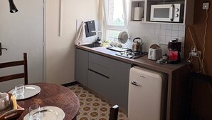 A compact kitchen with a dining table, chairs, a small refrigerator, a microwave, and a kettle.