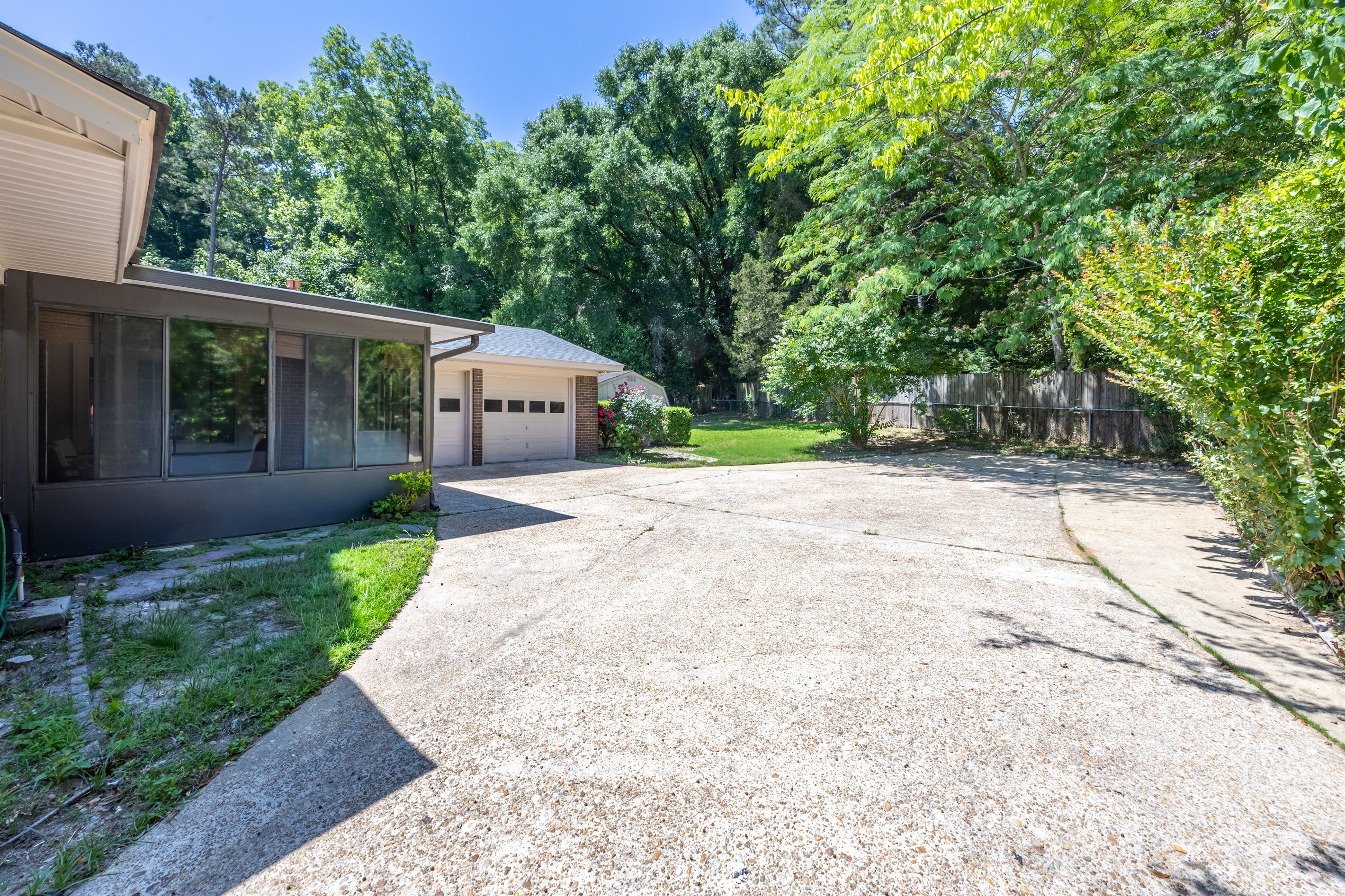A residential driveway leading to a house with a garage, surrounded by trees and a wooden fence.