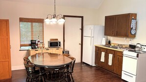 A compact kitchen with a dining table, wooden cabinets, and a refrigerator. - Golf • Fish • Hike • Located between Higgins & Houghton Lake (Roscommon)
